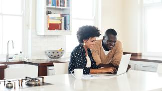 two people sitting at the dining room table looking at a laptop and smiling